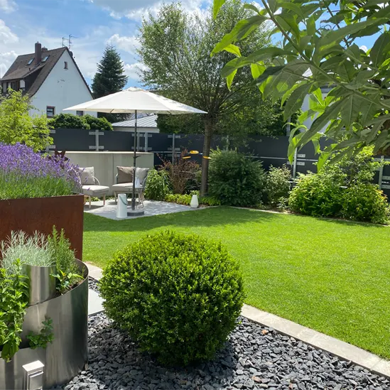 Moderne Gartenanlage mit gepflegtem Rasen, Sitzbereich unter einem Sonnenschirm, dekorativen Pflanzkübeln und Zierkiesflächen.