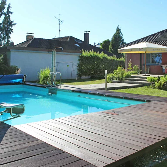 Elegante Poolanlage mit Holzdeck, umgeben von gepflegtem Garten und Terrasse, ideal für private Entspannung im Freien.