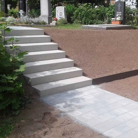 Neu angelegte Treppe und Gehweg mit Pflastersteinen, eingebettet in eine Grünanlage neben einem Friedhof.
